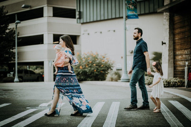 a stylish family crosses the street_ the mother wears a long dress and holds a baby, crosswalking 4k