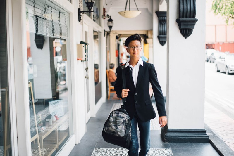 an asian man walking down the street holding a camouflage duffel bag, asian man and duffel 4k