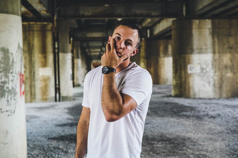 a man in a white t shirt with his hand on his face beneath a bridge, shameless 4k