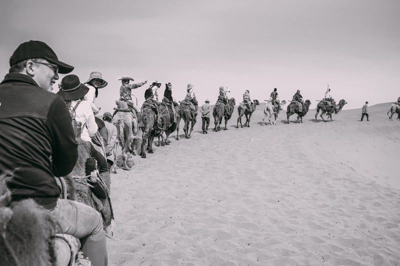a group of tourists rides a line of camels in the desert with guides on foot, tourists riding camels 4k