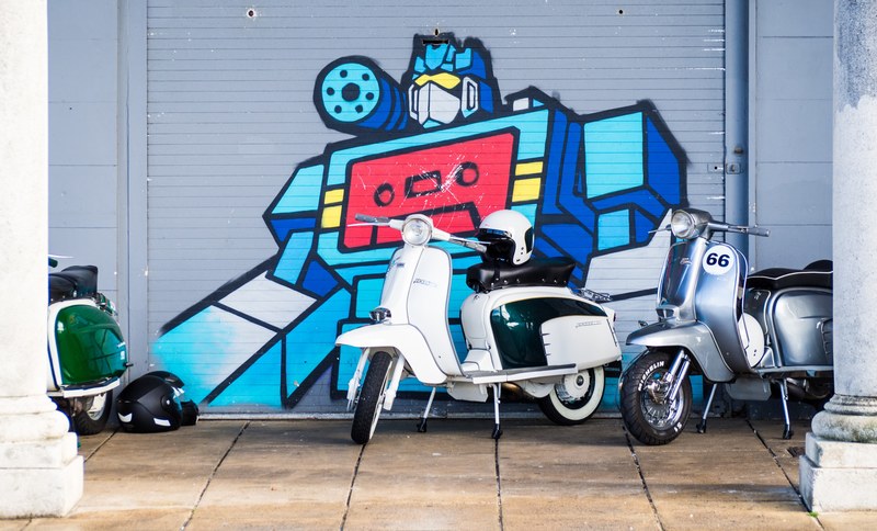 group of vespa scooters on sidewalk parked in front of optimus prime robot from transformers graffiti mural, scooters in front of graffiti 4k