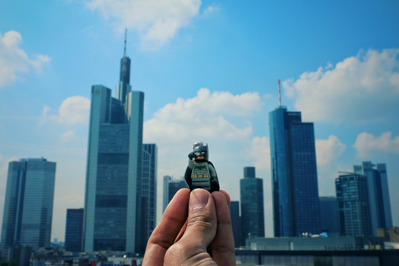a person holding a lego guy toy in the air with his fingers with skyscrapers and a cloudy sky in the background, _holding up lego guy outside 4k