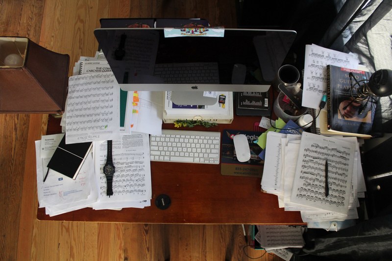 drone view of messy desk with piles of sheet music and mac desktop computer and keyboard, music 4k