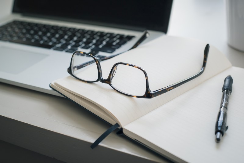 a pair of glasses and a pen on an open notebook next to a laptop, hard at work 4k