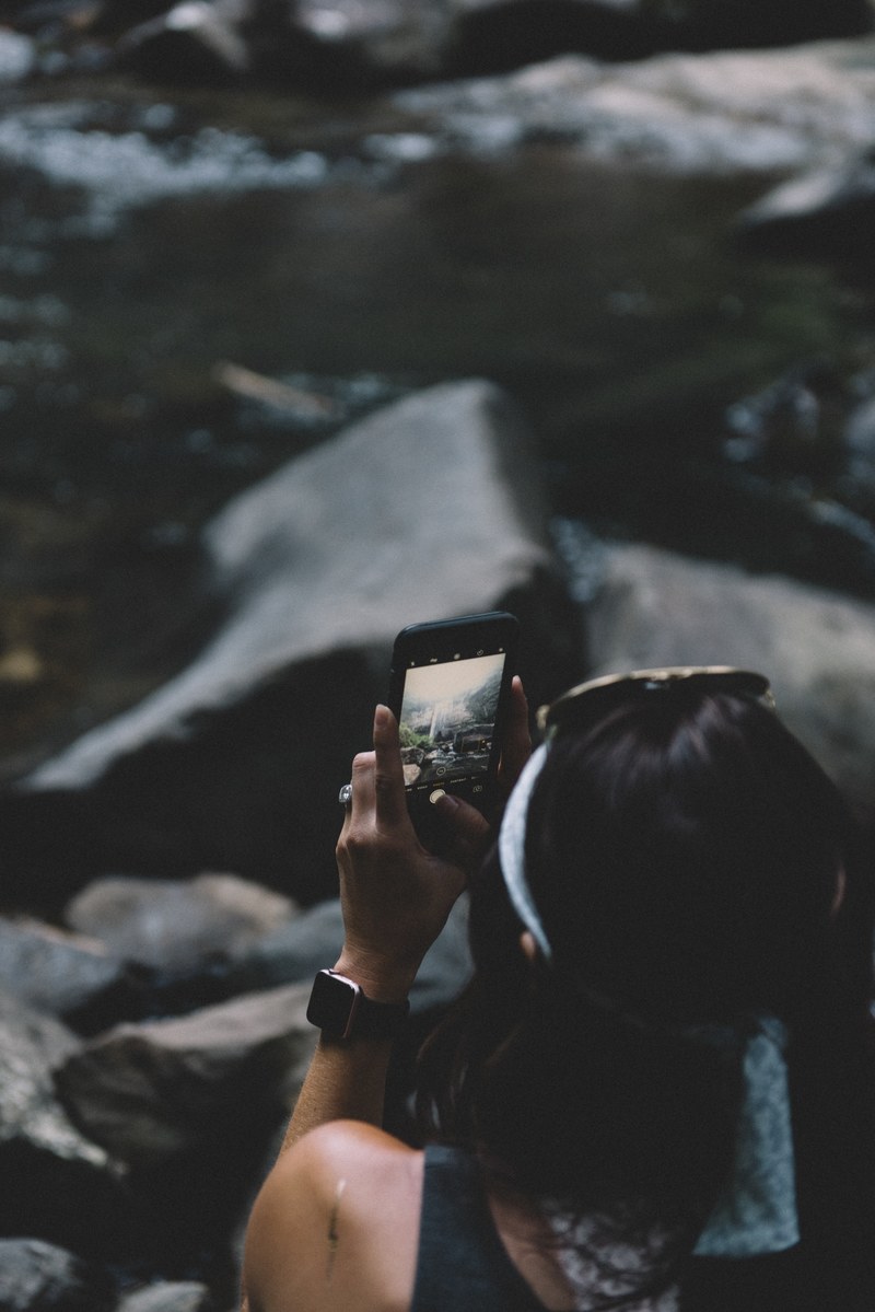 a woman sits on rocks in cloudland canyon state park taking a photo with an iphone, woman taking an iphone photo 4k