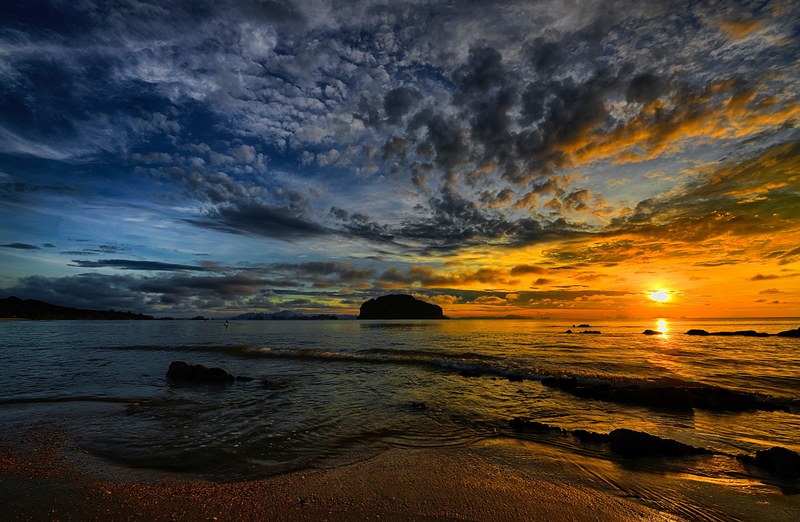 viewing the shoreline and the horizon in thailand as the calm sea breaks on the beach one silhouette island in the distance and a richly colored blue and orange sky including broken cloud du 4k