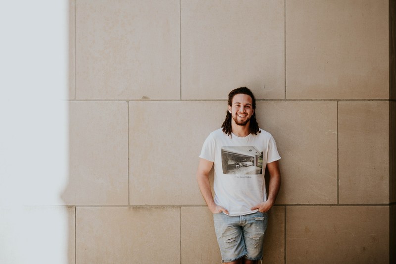 a man wearing a t shirt and denim cutoff shorts, man leaning against wall 4k