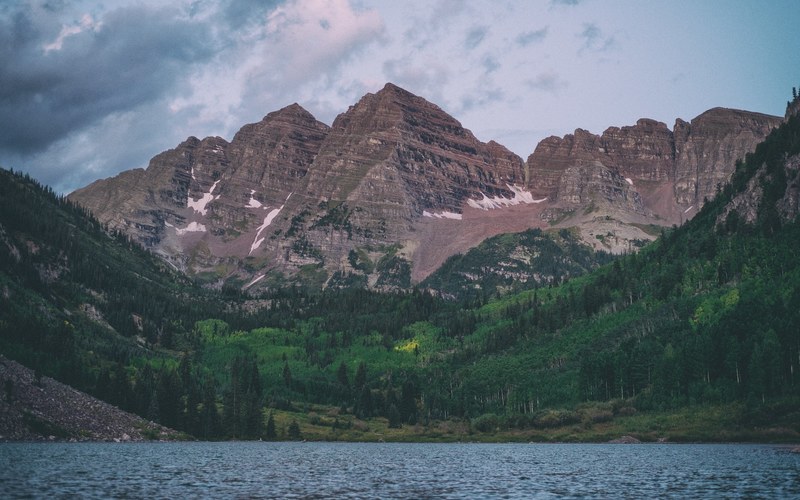 two red hued mountain peaks towering above a green forest and a lake in maroon bells, maroon bells peaks and a lake 4k