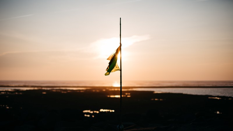 a flag at half mast on a flat shoreline with the sun setting behind it in ars en r, _lost flag 4k