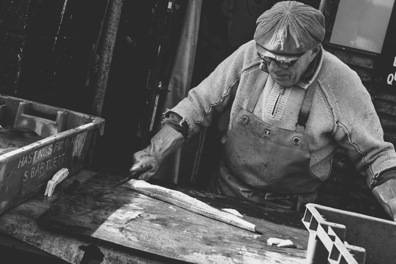 an old fisherman wearing an apron and a cap cutting a fish on a cutting board, old fisherman cutting fish_ 4k