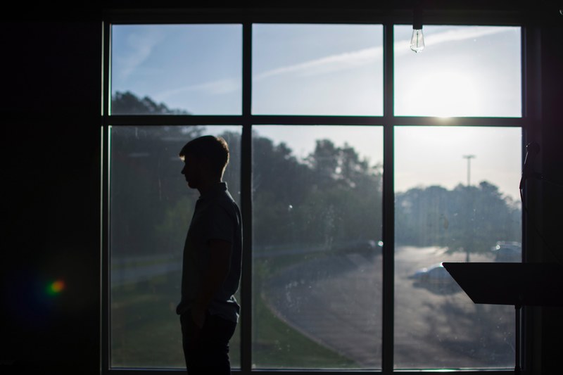 silhouette of a person in front of a window showing trees a street and sunlight, silhouette in front of window 4k