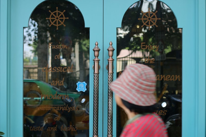 a woman in a hat standing in front of the door to a restaurant, blue restaurant door 4k