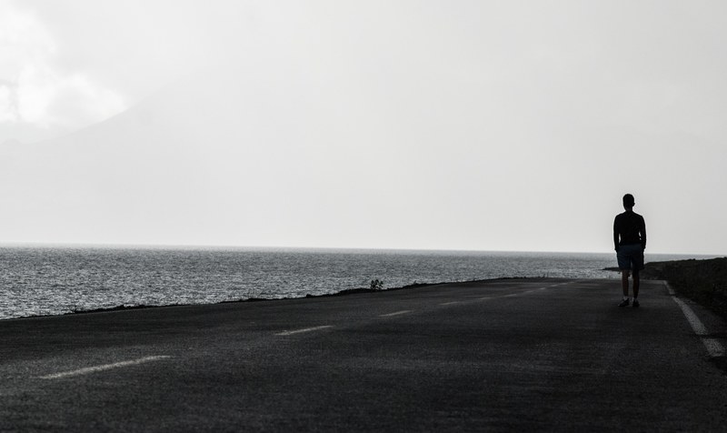 black and white shot of lonely person walking on road near sea with clear sky, lonely walk on sea road 4k