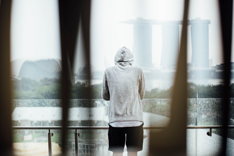 person in a hoodie standing on a balcony looking at singapore landmarks, standing on a balcony 4k