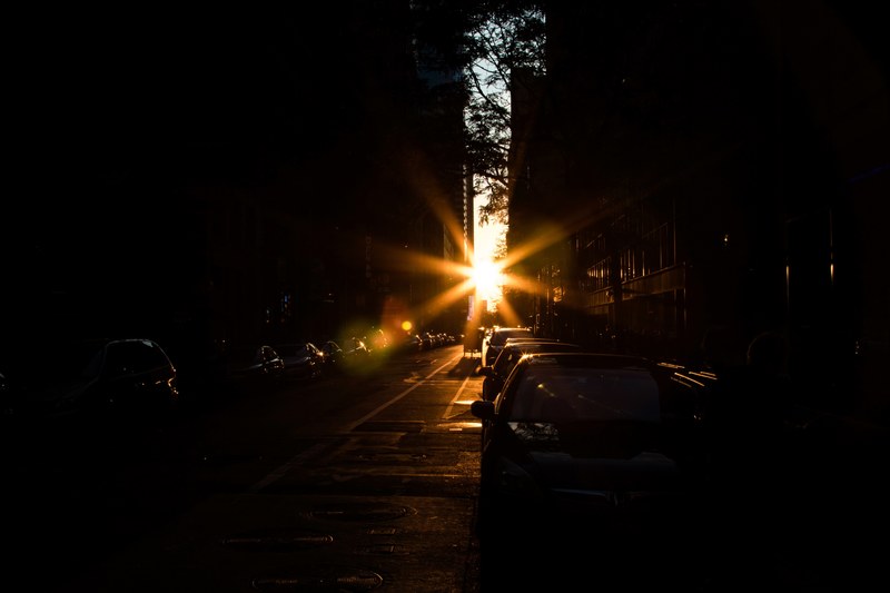 the sun glaring through between buildings on a dark street, _sunset between buildings 4k