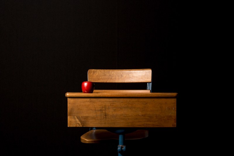 an apple on a wooden desk with attached chair in a black room, wooden desk and apple 4k