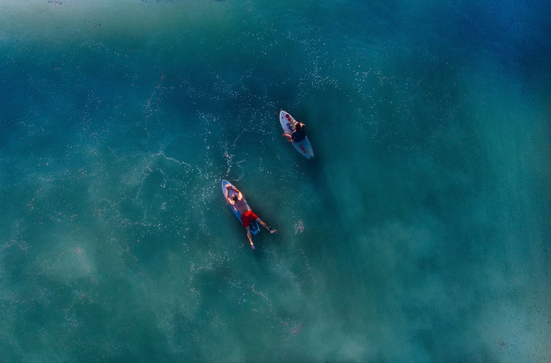 two surfers on their boards in the calm sea shot overhead by drone, calm blue sea surfing 4k