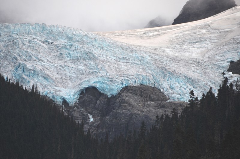 the jagged surface of a mountain glacier over a coniferous forest, icy blue mountain glacier 4k