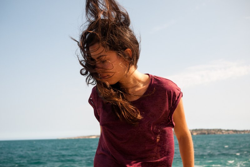 woman with hair blowing in the wind standing on the ocean shore, sicily_ 4k