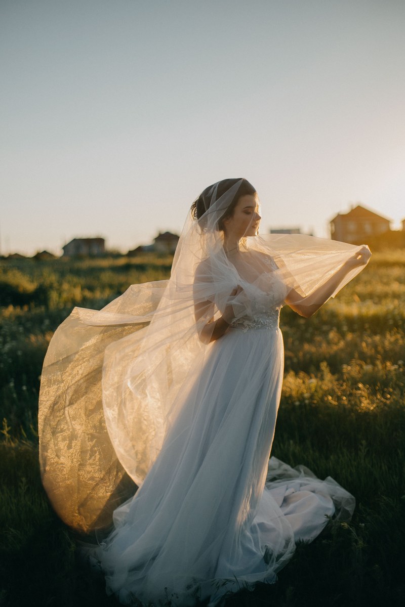 bride standing in a field in a wedding gown wth a veil wrapped around her, colors of love 4k