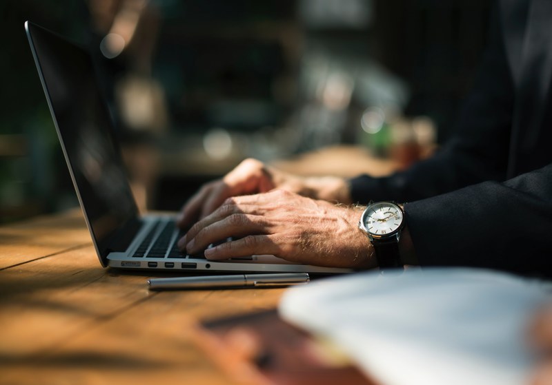 a person typing on their laptop while sitting at a picnic table, using laptop outside 4k