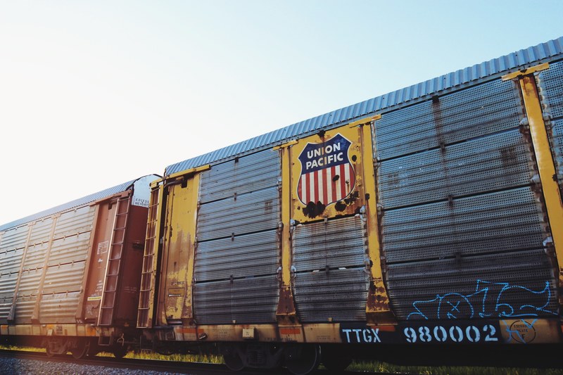 an old rusting union pacific railcar with blue graffiti on it passing a grassy area under a clear sky, union pacific freight car 4k
