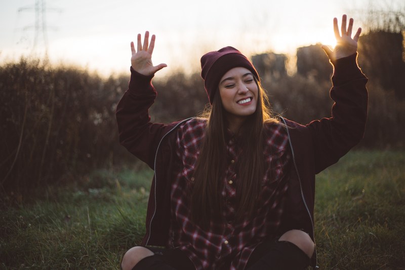 a happy woman sitting outside smiling with her hands raised to the sky, _catch the right light 4k