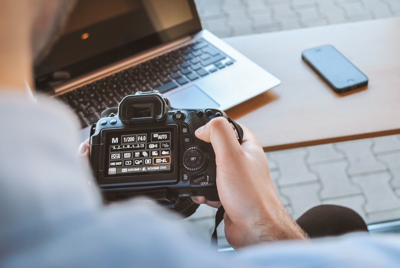 a person adjusting settings on a professional dslr camera near a table with a laptop and a phone on it, photographer working on his dslr camera in cafe 4k