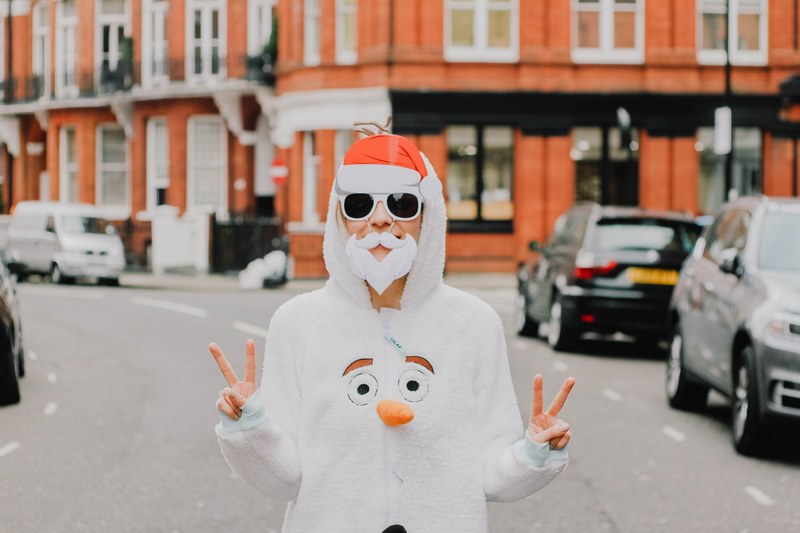 a person wearing a fake white beard and santa hat with a jumper suit that features a snowmans face on the chest, _olaf 4k
