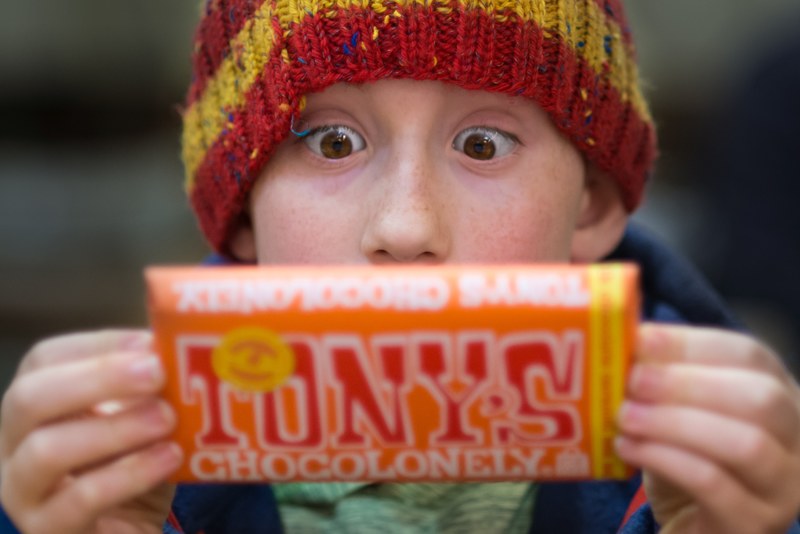 a little boy wearing a striped beanie reading the label of a chocolate bar in portland, a friend with chocolate 4k