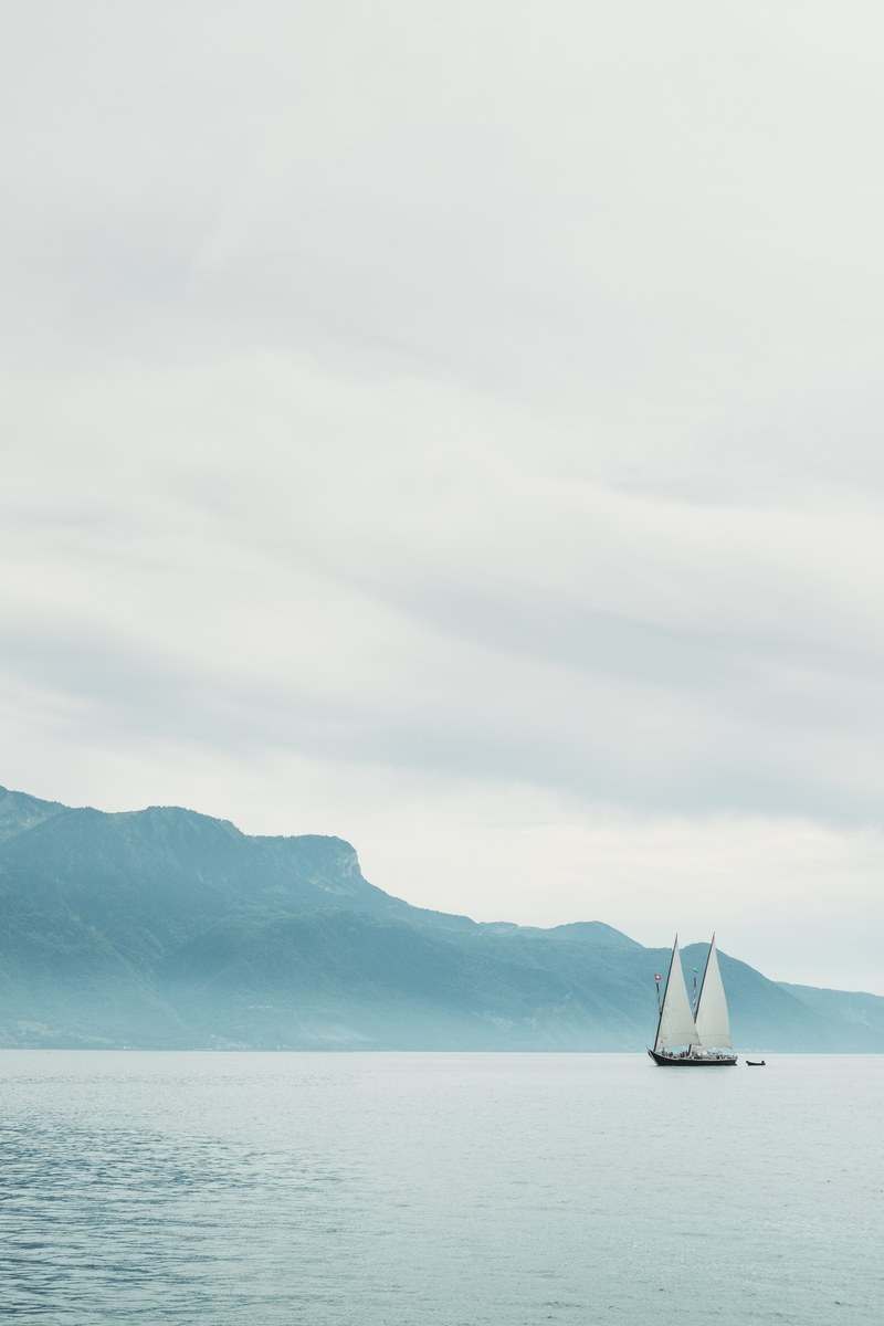 a sailboat floating in the water near a large mountain, _sailboat near mountain 4k