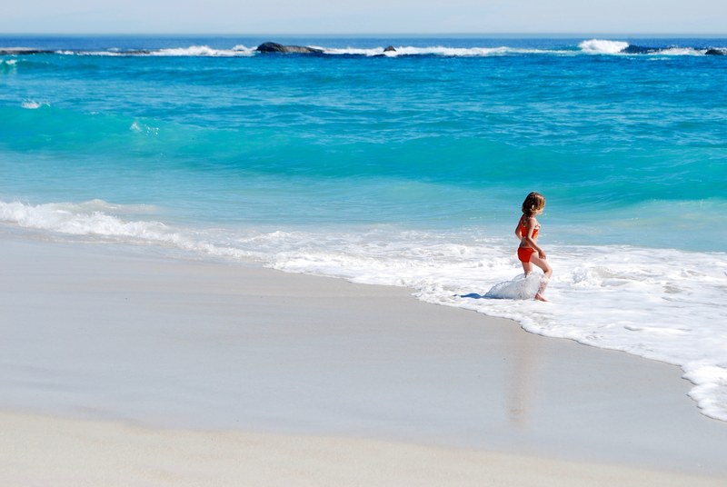a small girl playing in the small waves on the seashore, jumping over waves 4k
