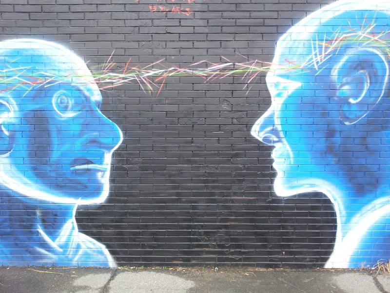 a brick wall mural of two cartoonish people staring at each other, _two blue heads staring mural 4k