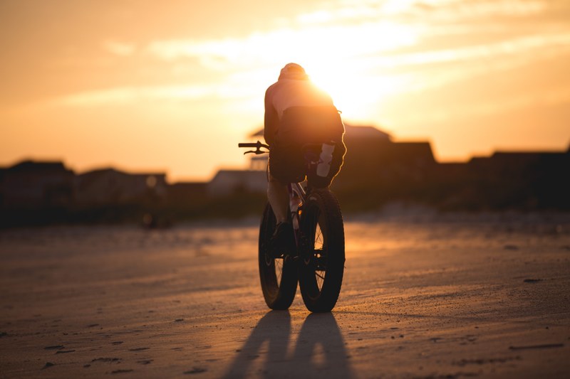 a shirtless man riding a bike with large tires with the sunset in the background, _beach biker 4k