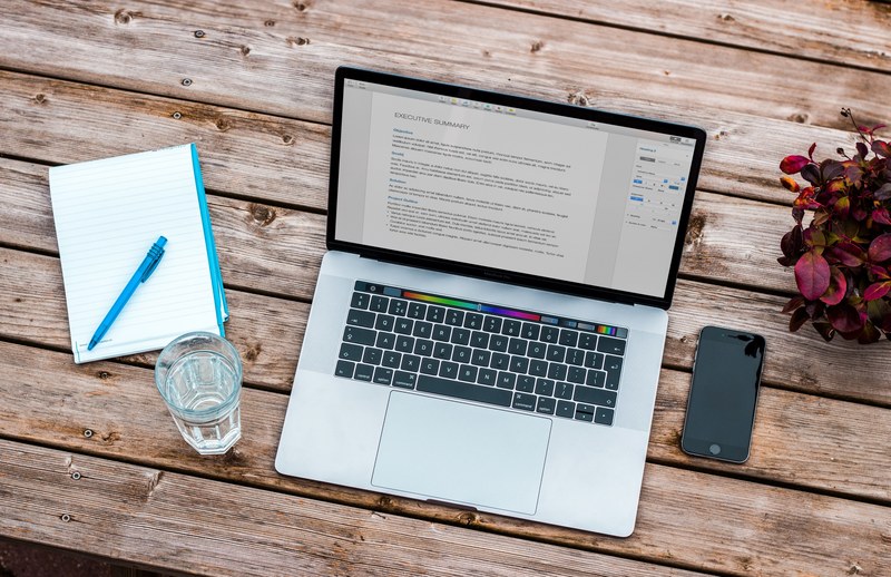 an overhead shot of a macbook with a draft of an executive summary on a wooden surface, macbook pro 2016 4k