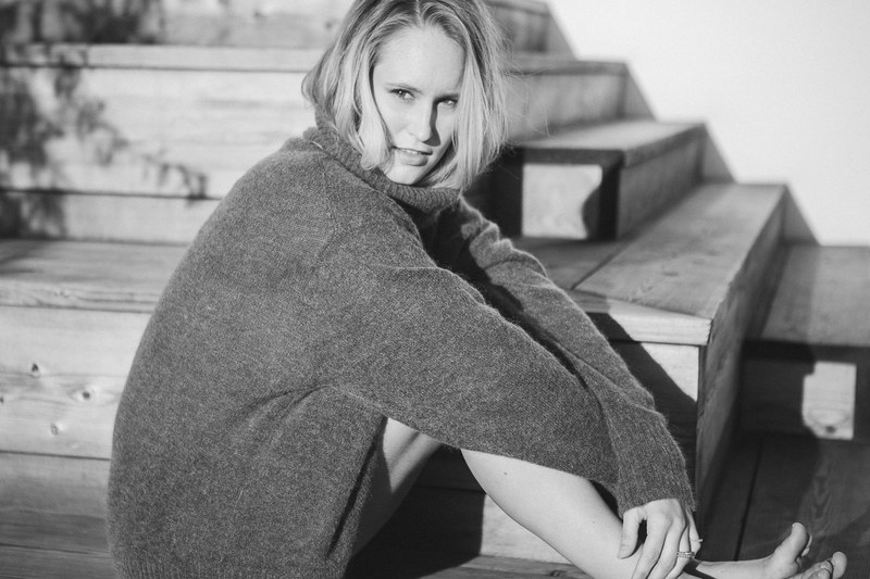 a black and white woman in a large sweater sits aside wooden stairs, woman aside wooden stairs 4k