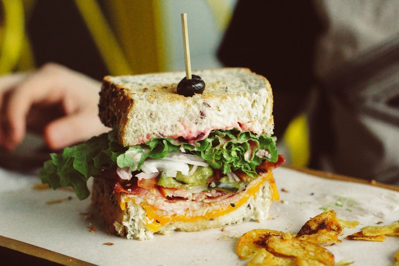 a sandwich with lettuce onion cheese and cold cut meat besides some chips, stacked handmade sandwich 4k