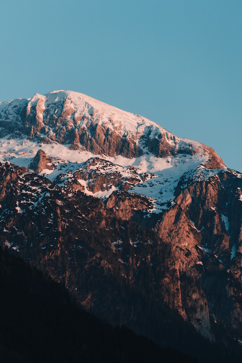 a steep craggy mountain face with its crest covered in snow in berchtesgaden, wild sunset 4k