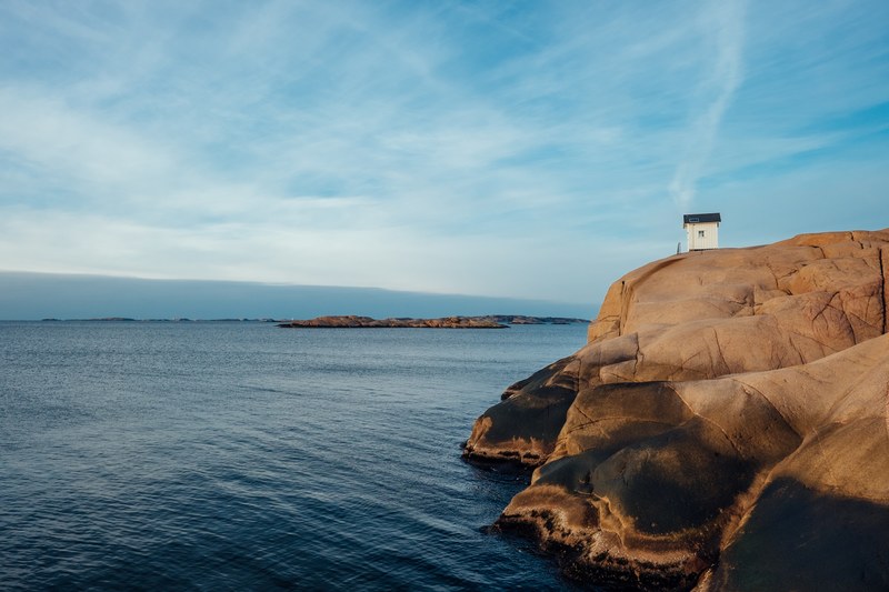 a white cabin on top of a smooth cliff over the choppy surface of the sea, cabin on the cliff 4k
