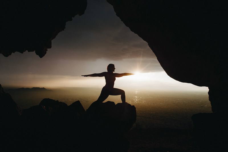 a person does yoga at a cave mouth as the sun rises in front over a calm sea, yoga sunrise_ 4k