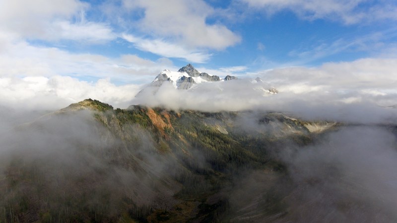 clouds enveloping snowy peaks towering over forested valleys in the mount baker national forest, white clouds around snowy mountains 4k