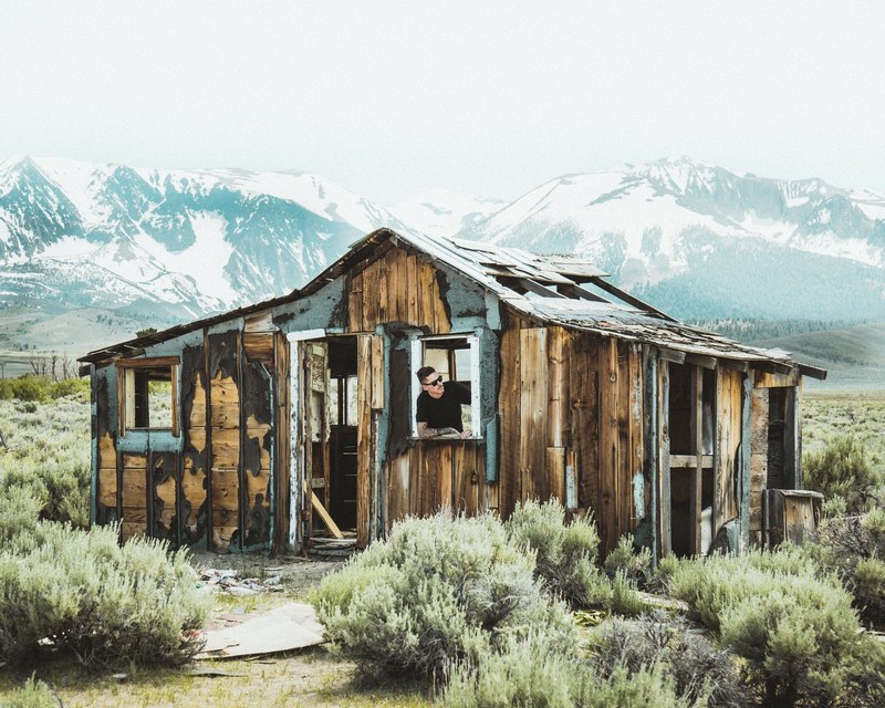 a man in sunglasses looks out of a dilapidated cabin in the mountains, mountain shack 4k