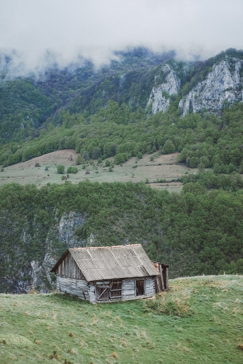 a dilapidated cabin on a grassy hill in the mountains, abandoned cabin on a hill 4k