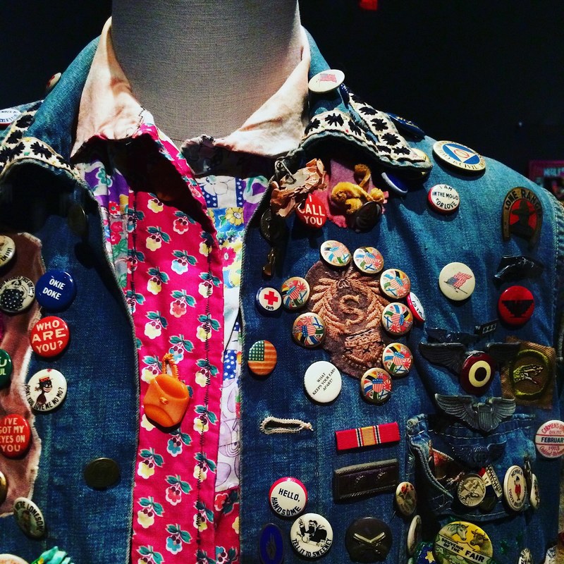 a dummy with a colorful button up shirt and jean jacket covered in pins at a museum, summer of love denim 4k