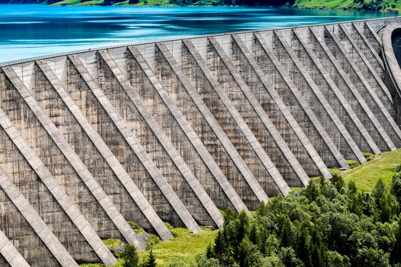 large concrete dam with foundational stanchions green grass trees and clear blue water, dam water green trees 4k