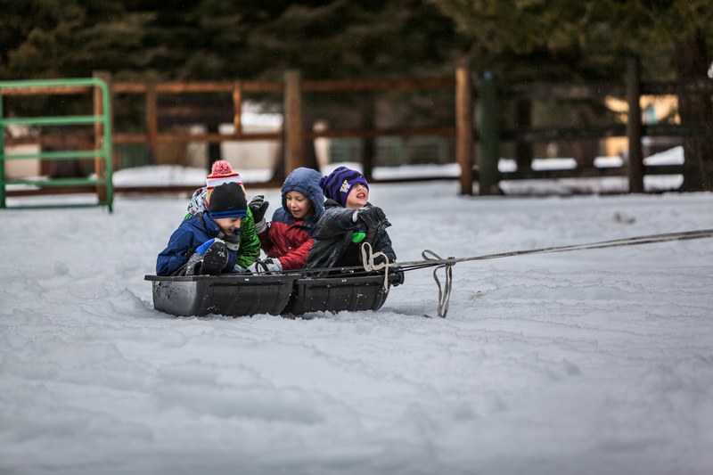 children riding on a sled pulled by a rope in a fenced area in the cold, snowboys 4k
