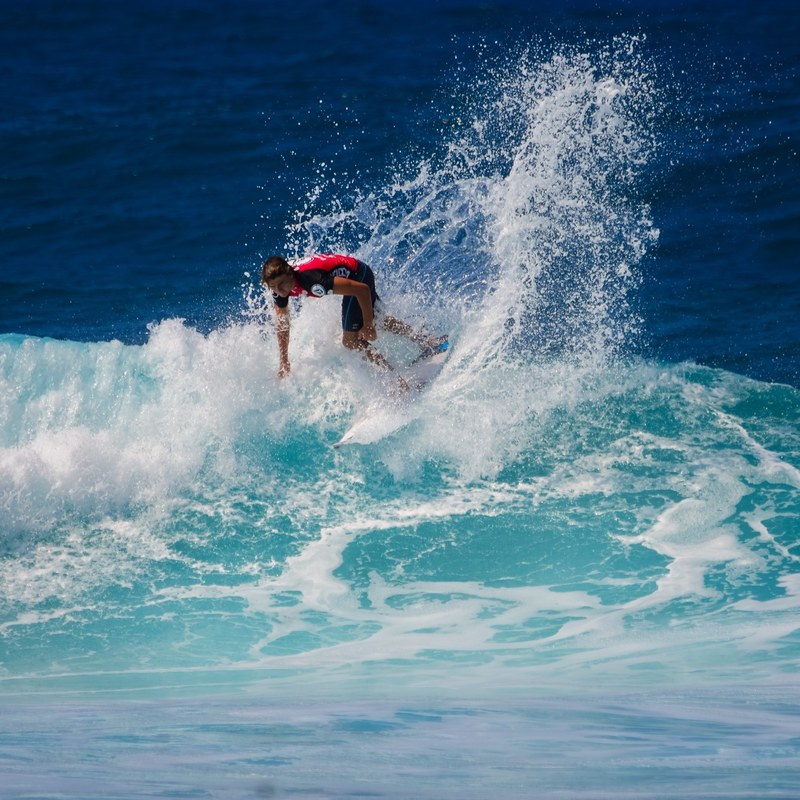a surfer in a red wetsuit riding a wave in a clear blue ocean, adrenaline 4k