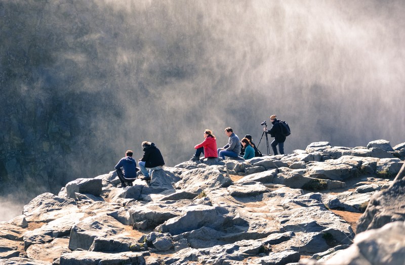 group of adventurers resting on rocks admiring and photographing the beauty of a mountain mist, adventurers taking a break 4k