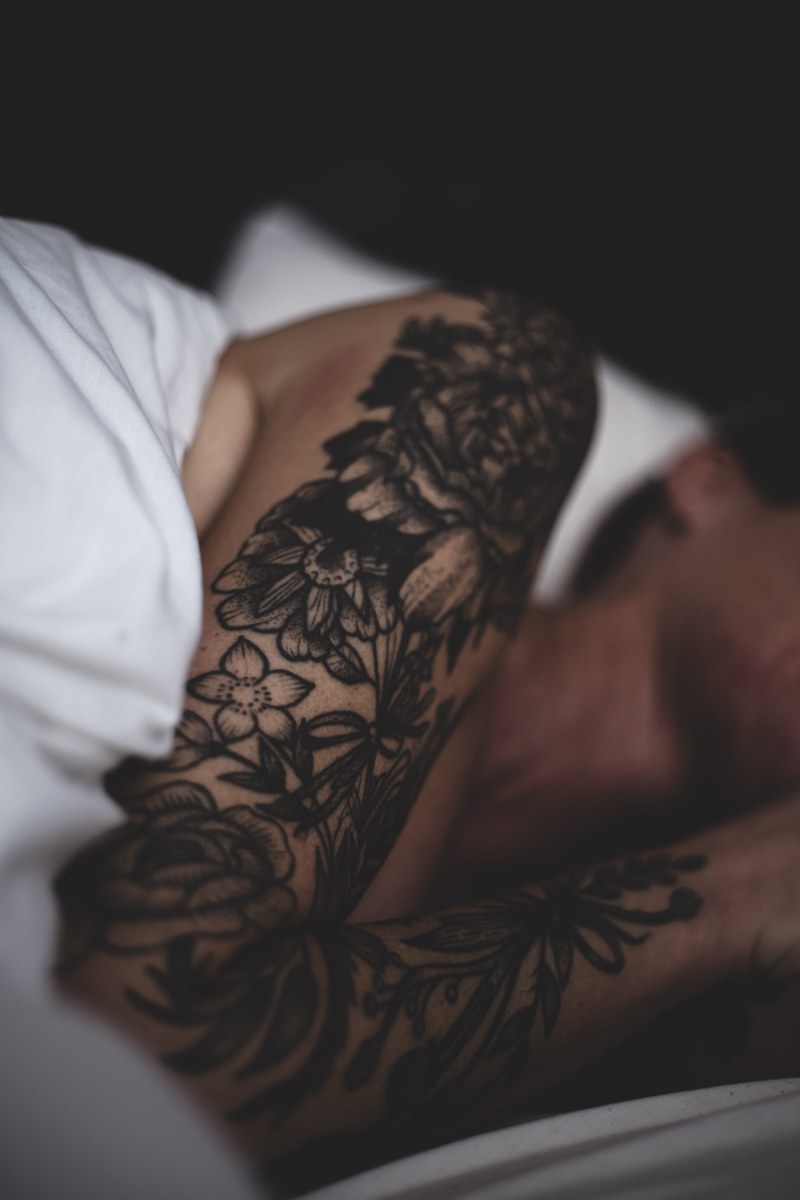 man with flower tattoos on his arm sleeping under white sheets on a bed in scotland, awakening 4k