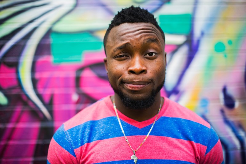 a man in a pink and blue striped shirt and africa necklace stands before a graffitied wall, man before graffitied wall 4k